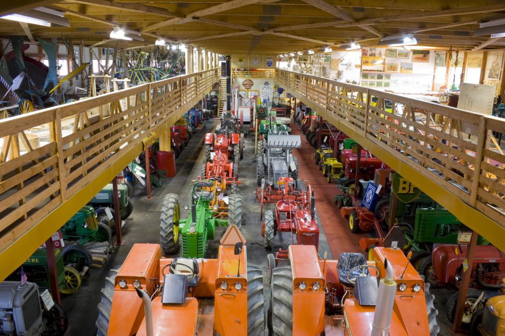 Iso kaksikerroksinen halli täynnä traktoreita ja maanviljelyyn tarkoitettuja välineitä Gårdskullan maatalousmuseossa.
