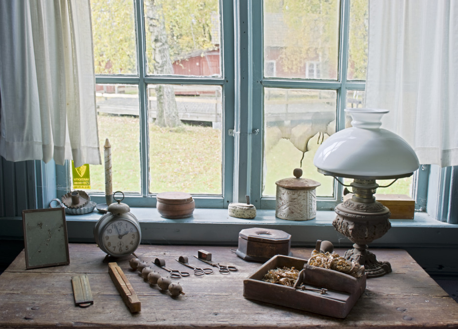 Pöytä, jossa vanhoja esineitä kuten öljylamppu, ikkunan edessä Inkoon kotiseutumuseossa.