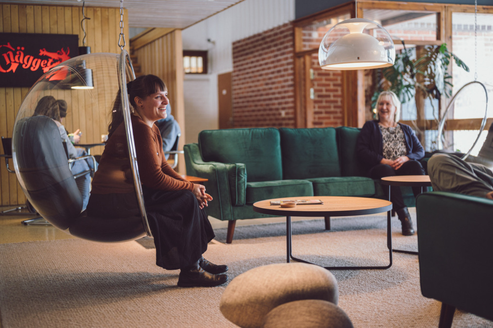 Kaksi naista istuvat loungetilan istuinryhmässä, toinen Eero Aarnion tuolissa Kupla, roikkuva versio ja toinen samettisessa sohvassa.